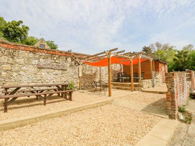 An outdoor seating area with wooden benches and chairs under orange shade sails and a stone wall with the sign The Lookout at Moonlight in Ventnor