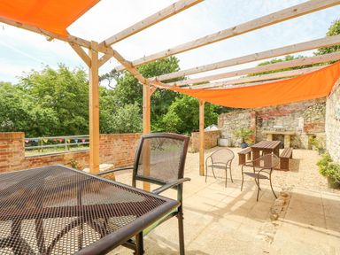 An outdoor patio area with metal and wooden chairs a wooden pergola with an orange canopy and a picnic table at Moonlight in Ventnor