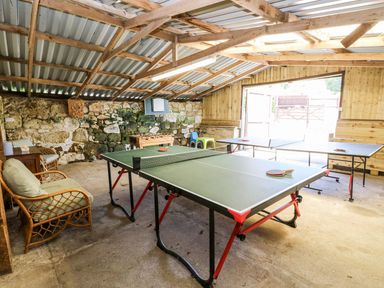 A game room with two table tennis tables a foosball table chairs and a stone wall at Moonlight in Ventnor