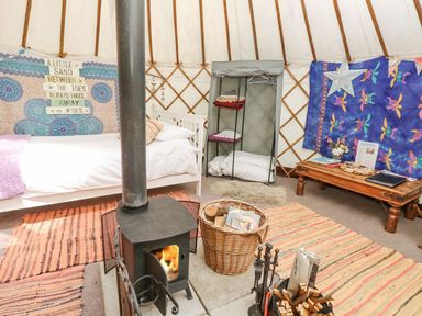 An interior of a yurt with a bed a wood burning stove a wicker basket with firewood a low wooden table and colorful tapestries at Stardust in Ventnor
