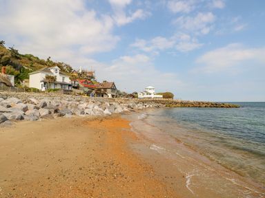 A sandy beach with rocks along the shore and houses on a hill near the coastline at Stardust in Ventnor