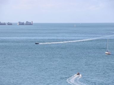 A seascape with several boats on the water and a group of rocks with a lighthouse in the distance at Stardust in Ventnor