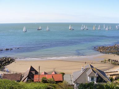 A sandy beach with people near houses and sailboats on the water at Stardust in Ventnor