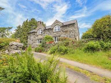 A stone cottage with arched windows surrounded by plants and trees at Dwynant in Bontddu near Dolgellau
