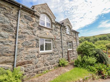 A stone cottage with leaded windows surrounded by greenery and a metal gate at Dwynant in Bontddu near Dolgellau
