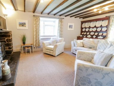 A living room with armchairs and a sofa near a window and a wooden cupboard with decorative plates at Dwynant in Bontddu near Dolgellau
