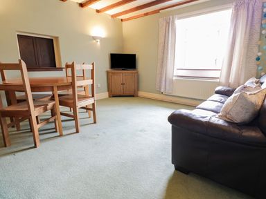 A living room with wooden dining table and chairs a leather sofa tv on a cabinet and a window with curtains at Dwynant in Bontddu near Dolgellau