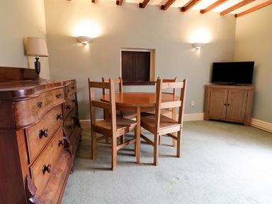 A dining area with a round wooden table and four wooden chairs a wooden sideboard with a lamp and a wooden cabinet with a television at Dwynant in Bontddu near Dolgellau