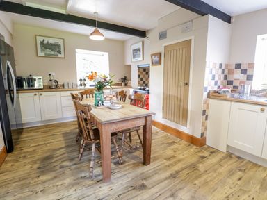 A kitchen with wooden dining table and chairs flowers on table and appliances on counters at Dwynant in Bontddu near Dolgellau