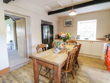 A kitchen with a wooden dining table and chairs next to a black refrigerator and cream cabinets at Dwynant in Bontddu near Dolgellau