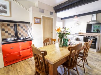 A kitchen with a wooden dining table and chairs a red stove and modern appliances at Dwynant in Bontddu near Dolgellau
