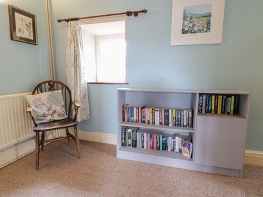 A wooden chair with a floral cushion next to a window with a curtain and a bookshelf filled with books against a blue wall at Dwynant in Bontddu near Dolgellau