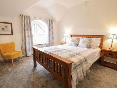 A bedroom with a wooden bed a yellow chair curtains on a window and bedside tables with lamps at Dwynant in Bontddu near Dolgellau