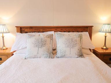 A bed with white bedding and tree-patterned pillows with wooden headboard and bedside tables with lamps at Dwynant in Bontddu near Dolgellau