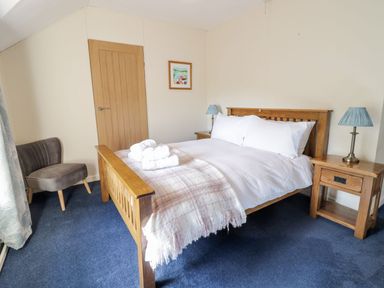 A bedroom with a wooden bed white bedding two bedside tables with lamps a chair and a door at Dwynant in Bontddu near Dolgellau
