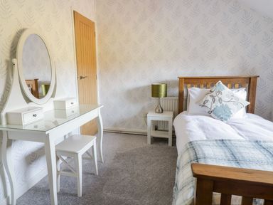 A bedroom with a wooden bed white dressing table with mirror and stool and a side table with lamp at Dwynant in Bontddu near Dolgellau