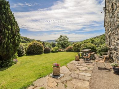 A garden with a stone patio bench and chairs next to a stone house at Dwynant in Bontddu near Dolgellau