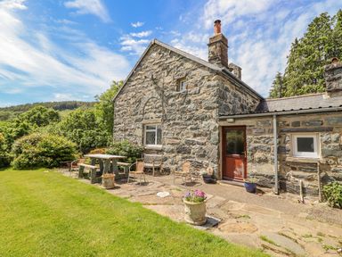 An outdoor patio area with chairs a bench and a picnic table next to a stone house at Dwynant in Bontddu near Dolgellau