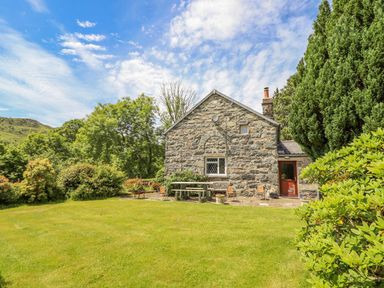 A stone cottage with outdoor chairs and table in a garden with trees and bushes at Dwynant in Bontddu near Dolgellau