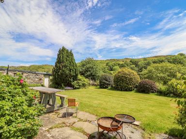A garden with a picnic table a chair and a fire pit surrounded by trees and bushes at Dwynant in Bontddu near Dolgellau