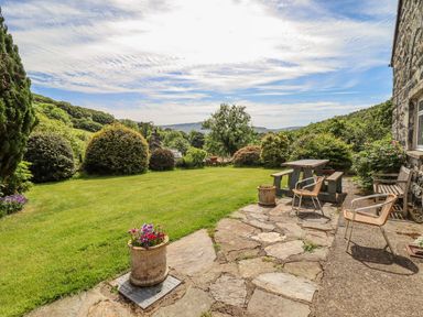 A backyard garden with a stone patio table bench chairs and flower pots at Dwynant in Bontddu near Dolgellau