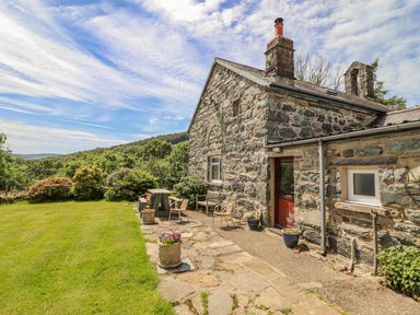 An outdoor patio area with chairs and a table next to a stone house surrounded by grass and bushes at Dwynant in Bontddu near Dolgellau