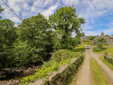 A country road next to a stone wall with plants and trees near stone houses at Dwynant in Bontddu near Dolgellau