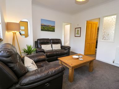 A living room with two leather sofas a wooden coffee table a floor lamp and wall art at Gilfach Bach in Dolgellau