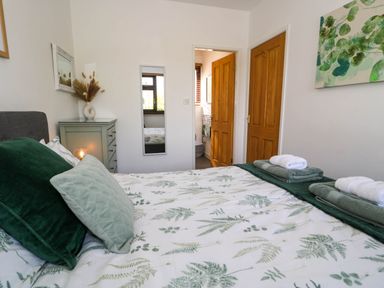 A bedroom with a bed with green and white botanical bedding two wooden doors a dresser with dried plants a mirror and a painting at Gilfach Bach in Dolgellau