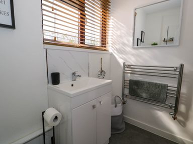 A bathroom with a white sink cabinet a window with wooden blinds a towel rail with a towel and a basket on the floor at Gilfach Bach in Dolgellau