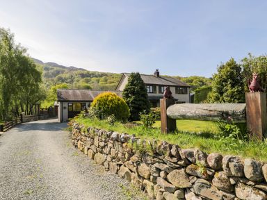 A gravel driveway leading to a house with a stone wall and trees at Gilfach Bach in Dolgellau