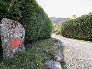 A gravel driveway lined with tall hedges and a stone marker with a red dragon and the word Gilfach at Gilfach Bach in Dolgellau