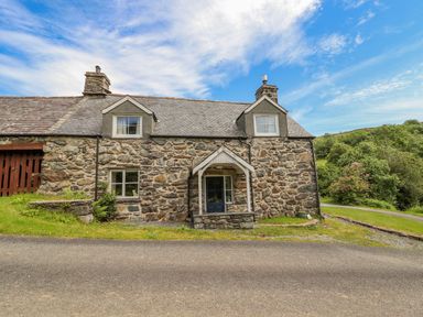 Stone cottage with two chimneys and a blue door by a paved road at Ty Glan Yr Afon in Bontddu near Dolgellau