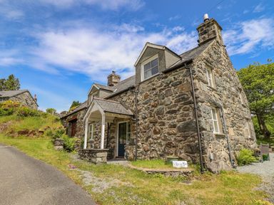 A stone cottage with a covered entrance and grass beside a paved road at Ty Glan Yr Afon in Bontddu near Dolgellau