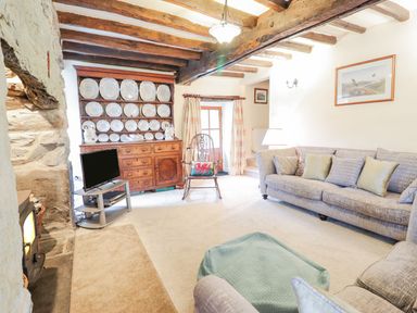 A living room with wooden beams a stone fireplace a wooden cabinet with plates a TV a rocking chair and sofas at Ty Glan Yr Afon in Bontddu near Dolgellau