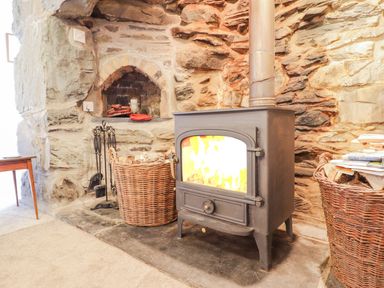 A wood burning stove with fire inside and baskets on each side in a room with stone walls at Ty Glan Yr Afon in Bontddu near Dolgellau