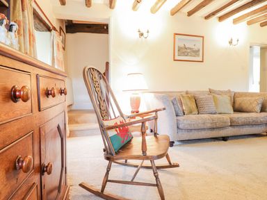 A living room with a wooden rocking chair with a cushion a sofa with multiple cushions a lamp on a small table and a wooden cabinet at Ty Glan Yr Afon in Bontddu near Dolgellau