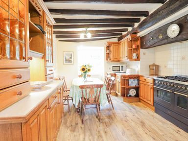 A kitchen with wooden cabinets a dining table with chairs and sunflowers in a vase at Ty Glan Yr Afon in Bontddu near Dolgellau
