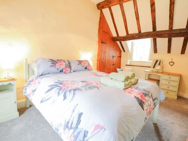 A bedroom with a double bed with floral bedding towels on the bed wooden beams on the ceiling a small dressing table and a nightstand at Ty Glan Yr Afon in Bontddu near Dolgellau