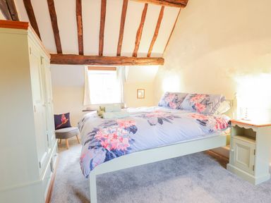 A bedroom with a bed with floral bedding a bedside table with a lamp a wardrobe a chair and wooden ceiling beams at Ty Glan Yr Afon in Bontddu near Dolgellau