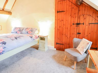 A bedroom with a bed floral bedding grey chair with flower cushion and wooden wardrobe at Ty Glan Yr Afon in Bontddu near Dolgellau