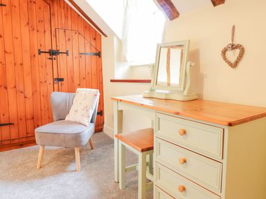 A room with a gray chair and a wooden dresser with a mirror at Ty Glan Yr Afon in Bontddu near Dolgellau