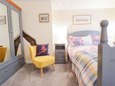 A bedroom with a grey bed a yellow chair with a bird cushion a grey wardrobe and bedside table at Ty Glan Yr Afon in Bontddu near Dolgellau