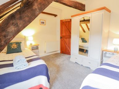 A bedroom with two single beds bedside tables lamps a wardrobe with a mirror and wooden beams at Ty Glan Yr Afon in Bontddu near Dolgellau