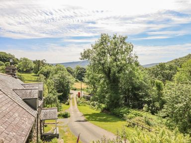 A rural road beside trees and a stone building with a slate roof at Ty Glan Yr Afon in Bontddu near Dolgellau