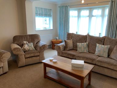 A living room with a sofa armchair wooden coffee table and curtains at Pen Y Frith Bungalow in Prestatyn