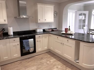 A kitchen with white cabinets black countertop and kitchen appliances at Pen Y Frith Bungalow in Prestatyn