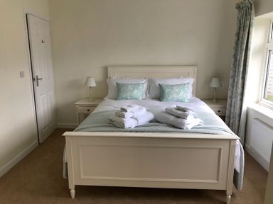 A bedroom with a double white bed with pillows and folded towels bedside tables with lamps and a window with curtains at Pen Y Frith Bungalow in Prestatyn