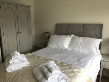 A bedroom with a double bed, bedside tables with lamps, folded towels on the bed, and a wardrobe at Pen Y Frith Bungalow in Prestatyn