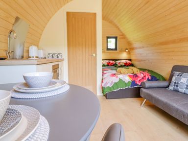 An interior with a kitchen area with dishes on a table a wooden door a bed with floral bedding and a gray sofa at Briallen in Bontddu near Dolgellau